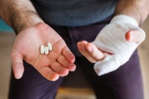Man with bandage on left hand and pills in right hand,